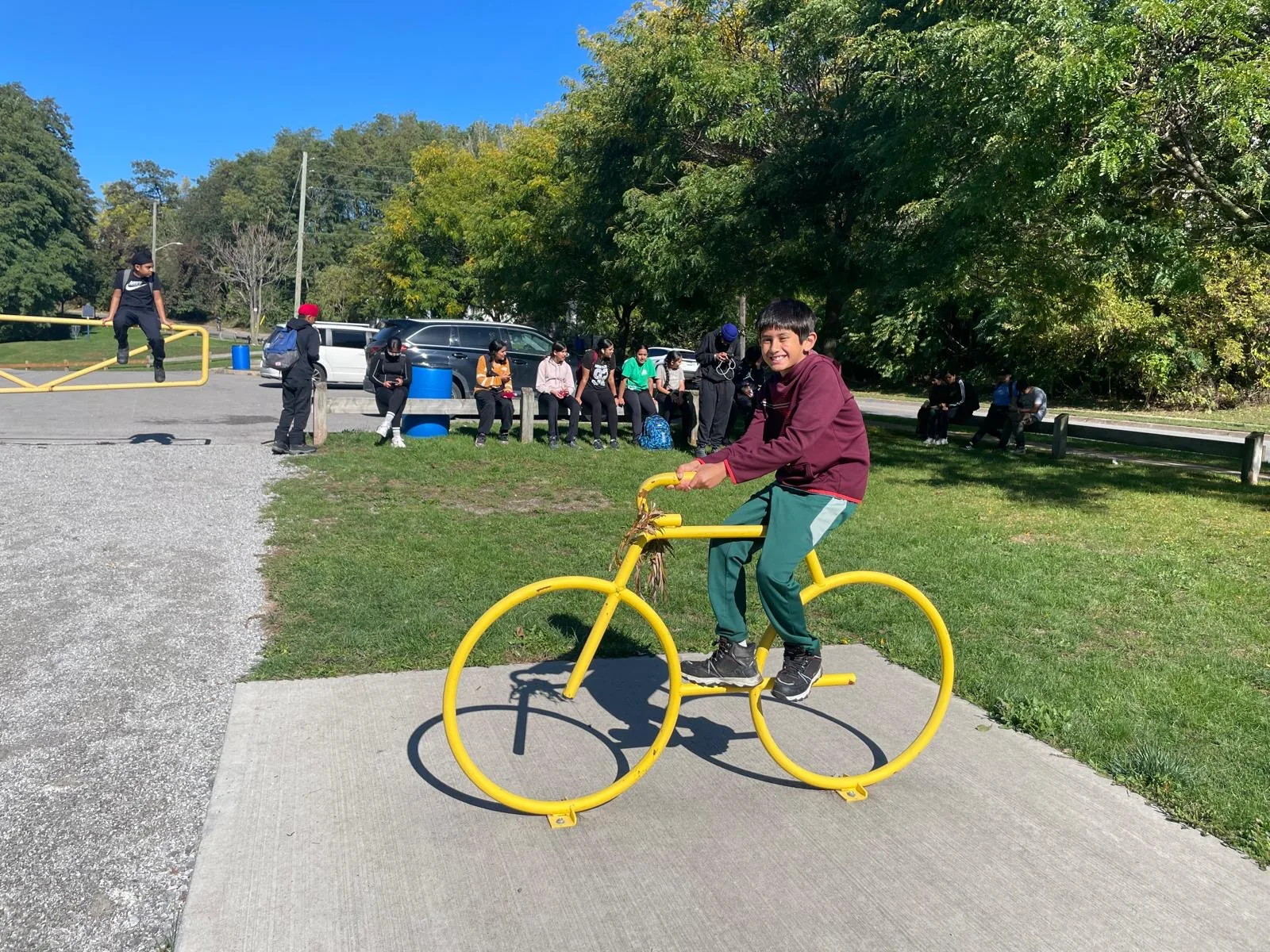 A young Progress Peel participant smiling on a yellow bike statue during an outdoor activity